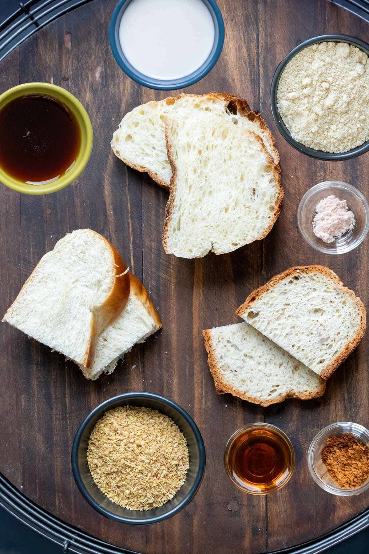 Piles of pairs of bread pieces on a wooden surface surrounded by bowls of ingredients to make the dip.