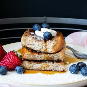 Three pieces of French toast in a pile with berries and butter on top.