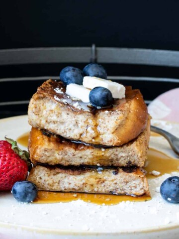 Three pieces of French toast in a pile with berries and butter on top.