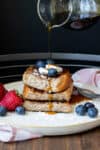 Pile of French toast on a cream plate with berries and maple syrup dripping on the top.