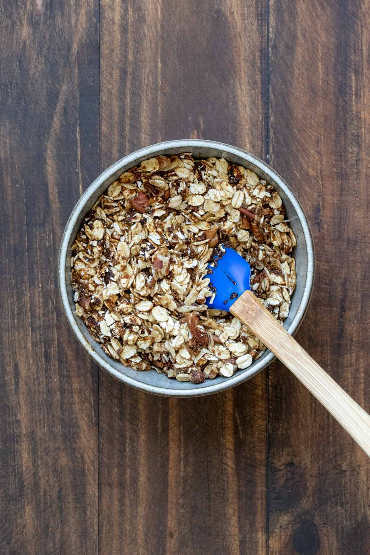 Spatula mixing oats, nuts and sugar in a grey bowl