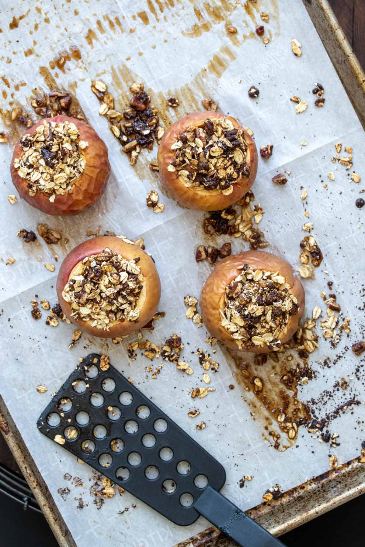 Black spatula next to four baked apples topped with oats