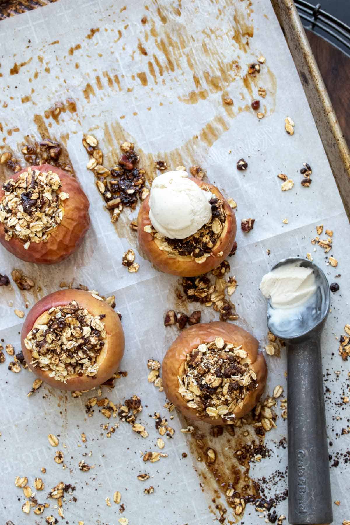 Top view of four baked apples on a piece of parchment with one topped with ice cream