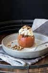 A whole baked apple topped with ice cream on a grey plate