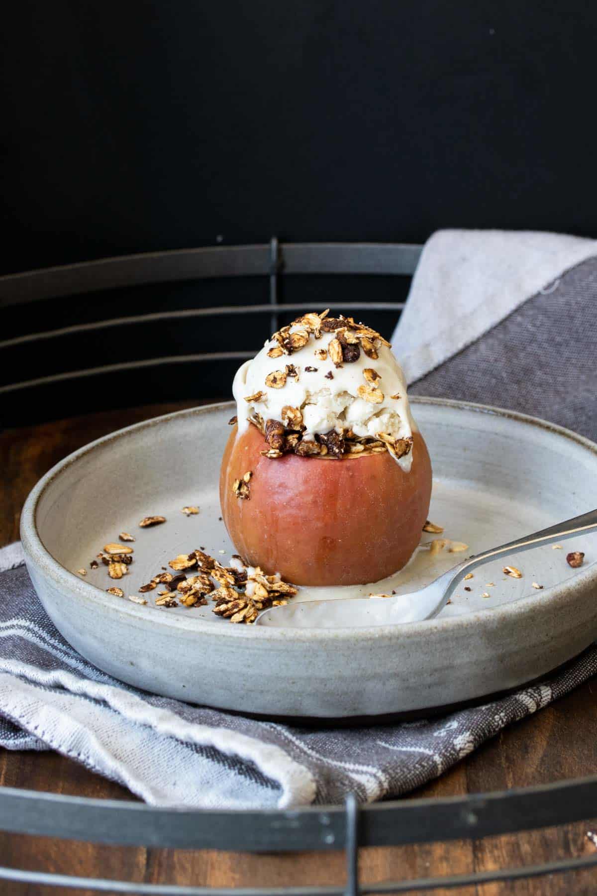 A whole baked apple topped with ice cream on a grey plate.
