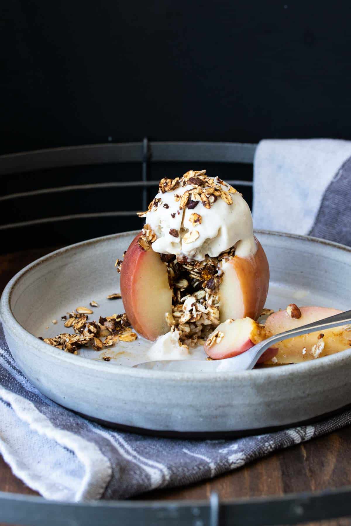 A baked apple with a piece out filled with oats on a grey plate.
