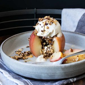 Fork taking a bite out of a baked apple on a plate.