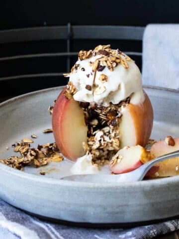 Fork taking a bite out of a baked apple on a plate.