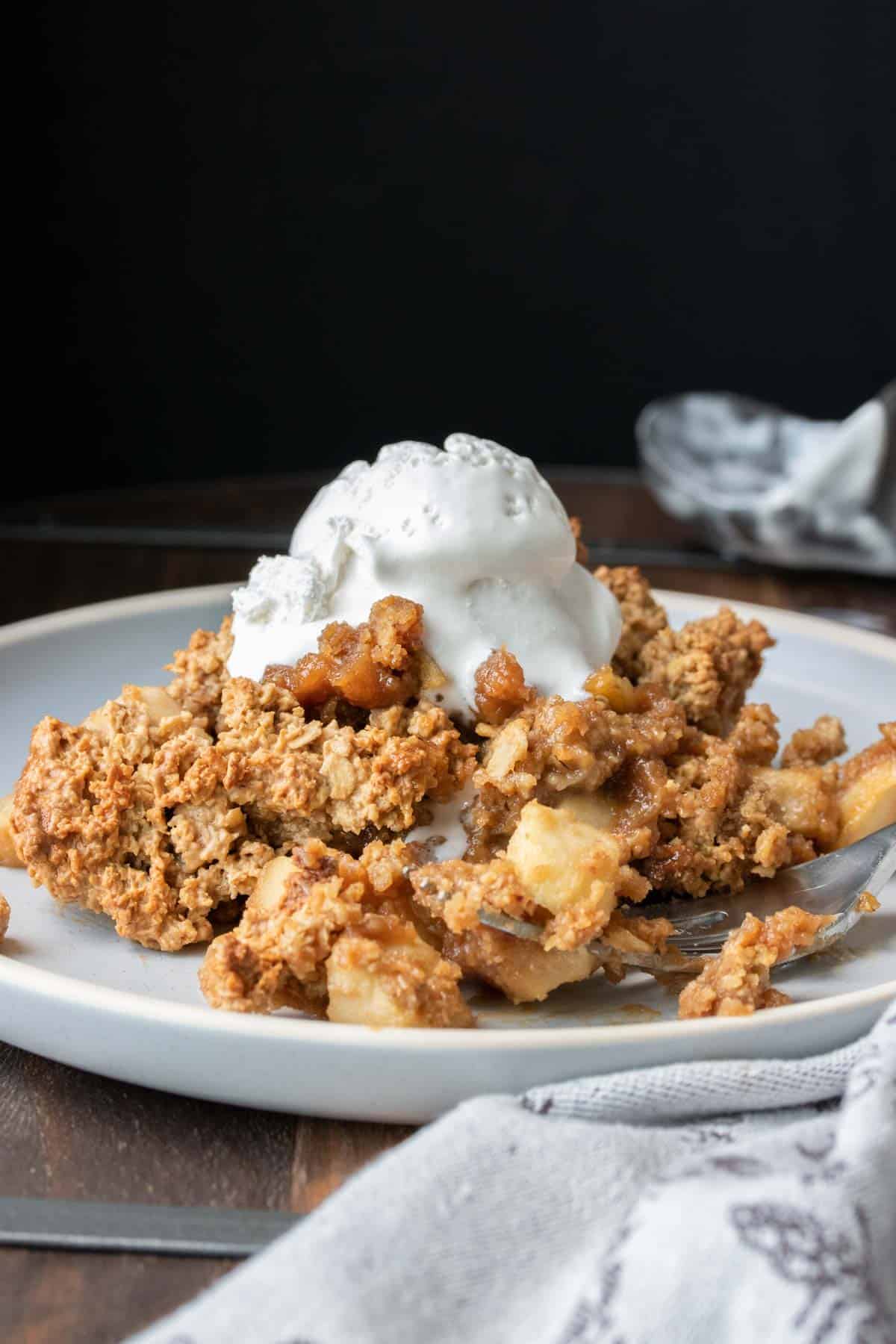 Side view of a wooden table with a plate of apple crisp and whipped cream