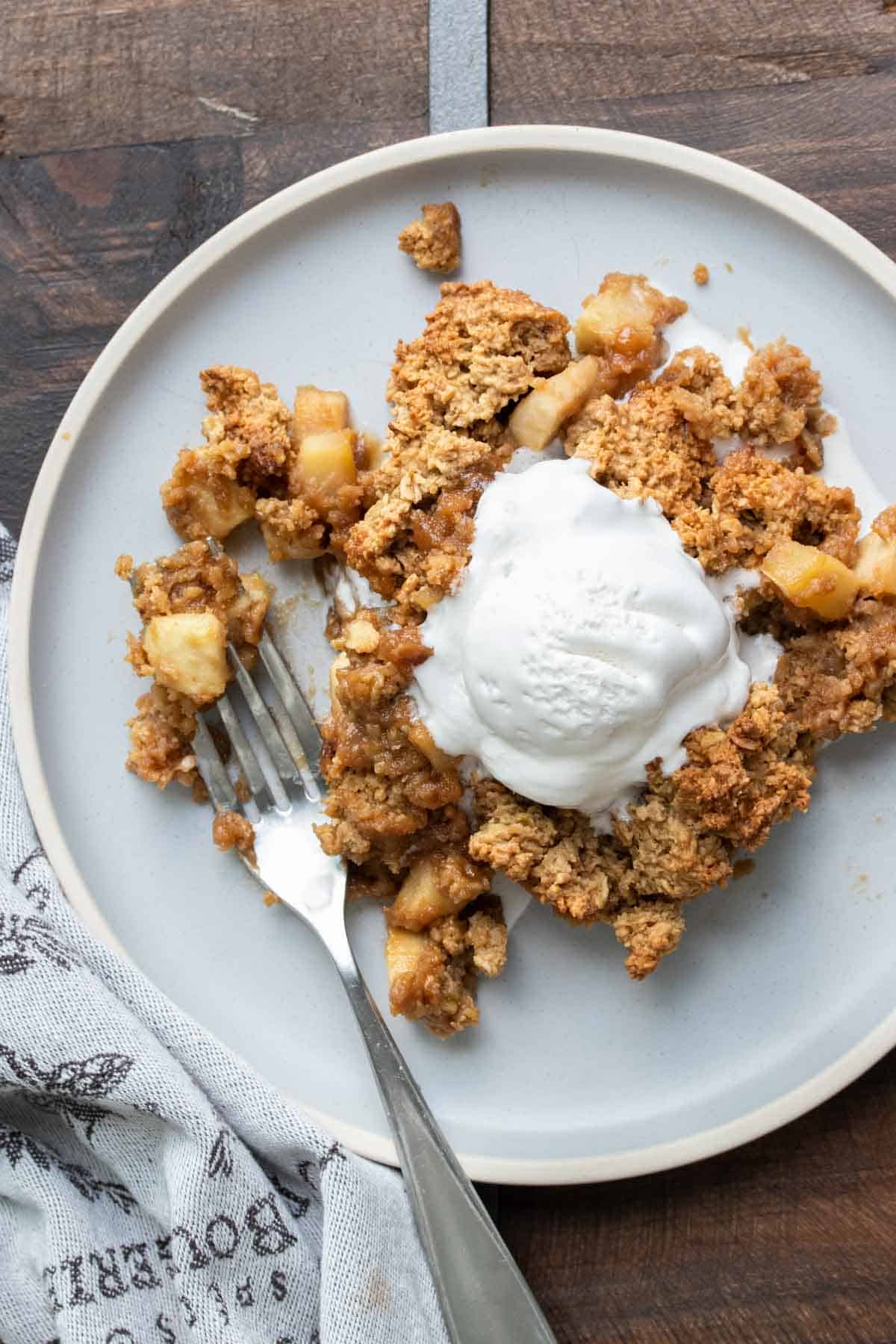 Fork taking a bite of apple crisp with whipped cream on a grey dish