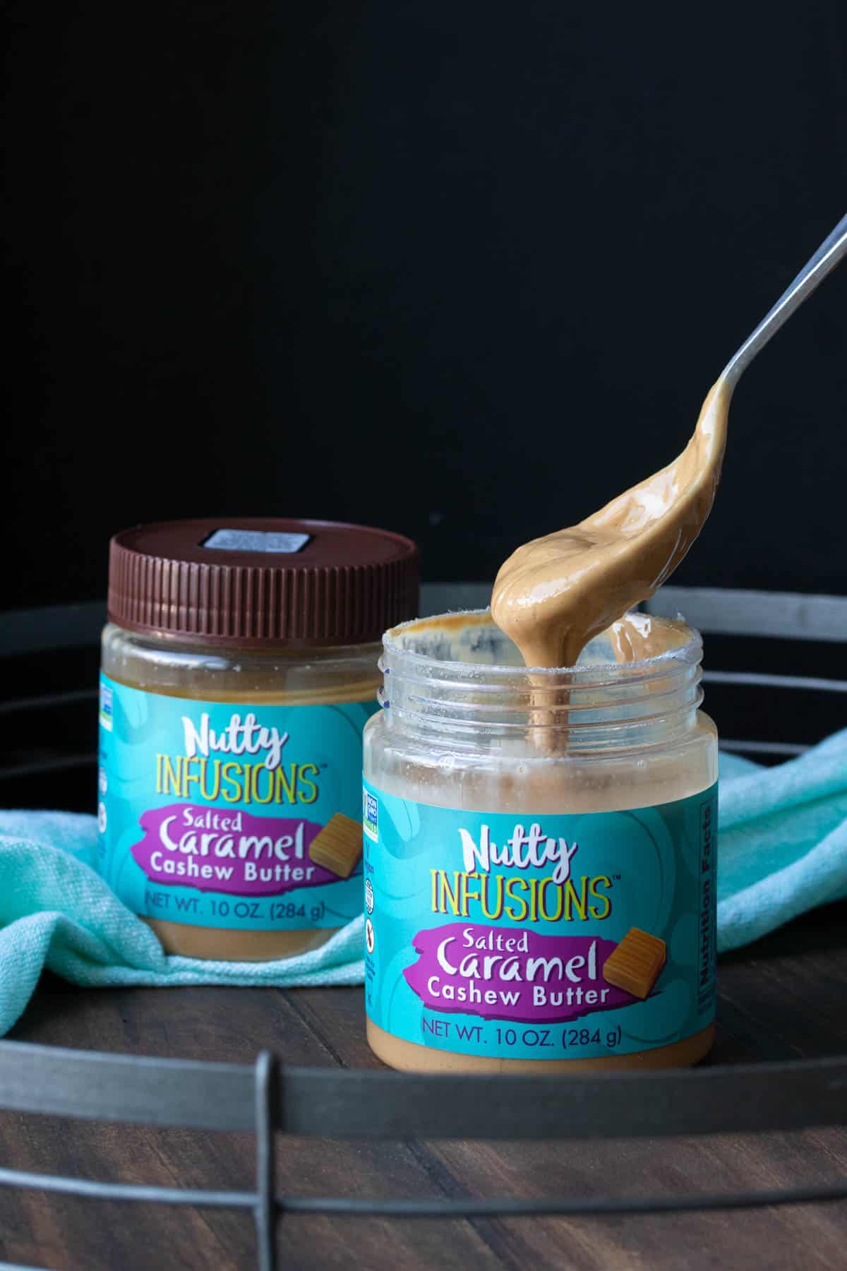 Spoon dripping cashew butter into a jar of cashew butter with a turquoise label.
