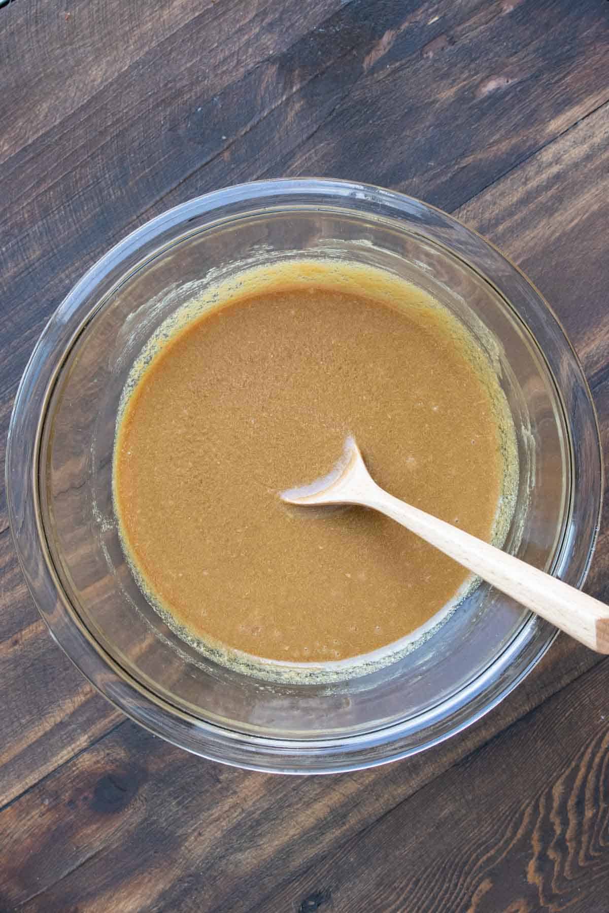 Wooden spoon mixing a caramel mixture in a glass bowl