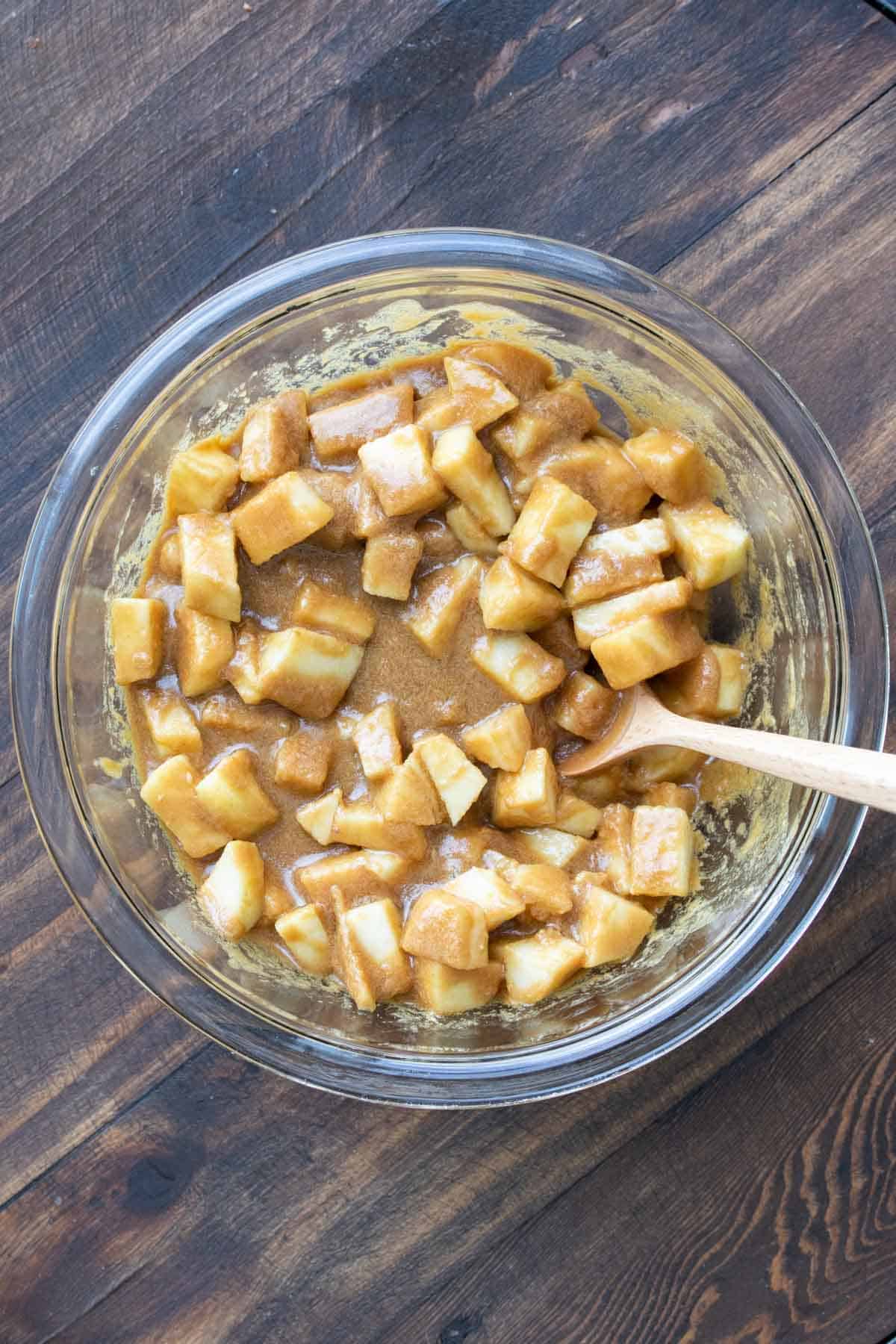 Spoon mixing apples and caramel mixture in a glass bowl.