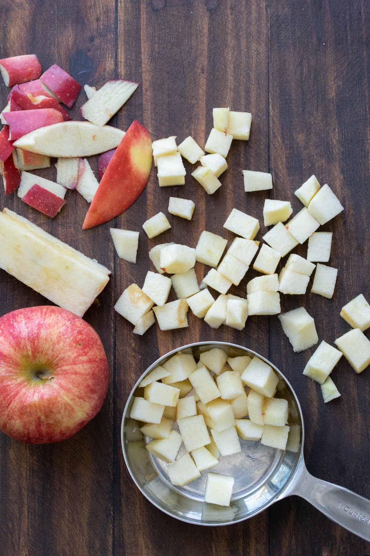 Pile of chopped apples in a measuring cup next to a whole apple.