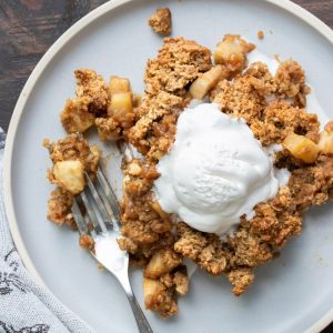 A piece of apple crisp on a grey plate with ice cream.