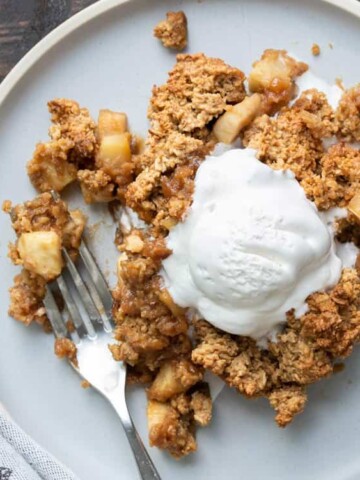 A piece of apple crisp on a grey plate with ice cream.