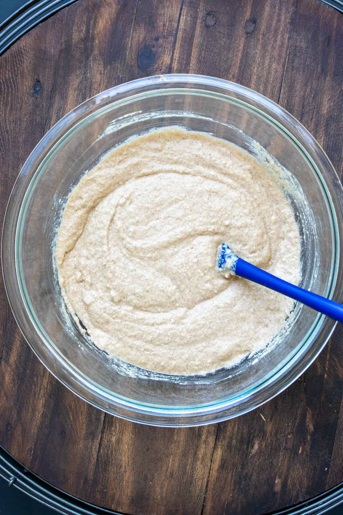 Blue spatula mixing a batter in a glass bowl.