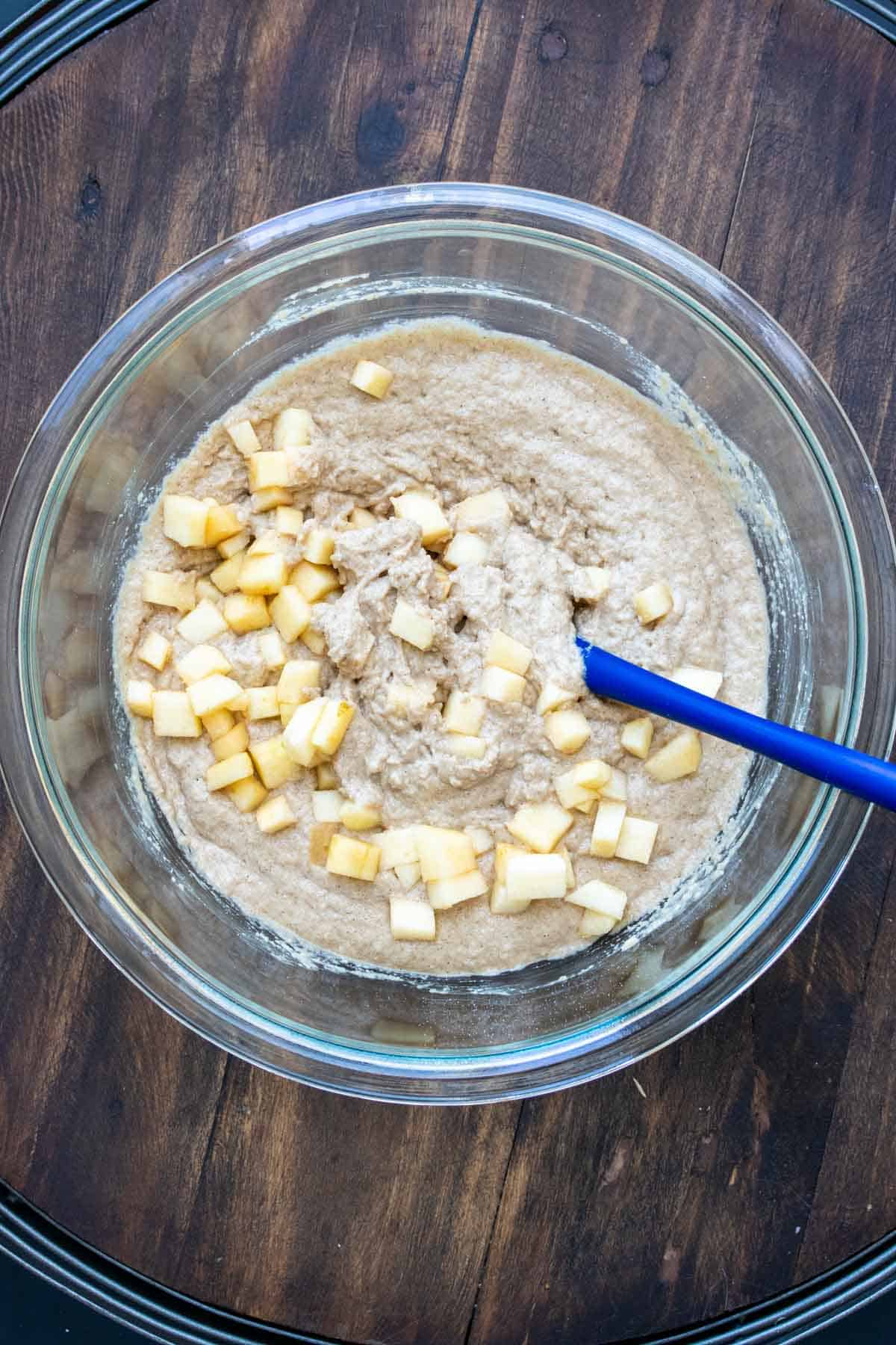 Batter with chopped apples being mixed in a glass bowl.