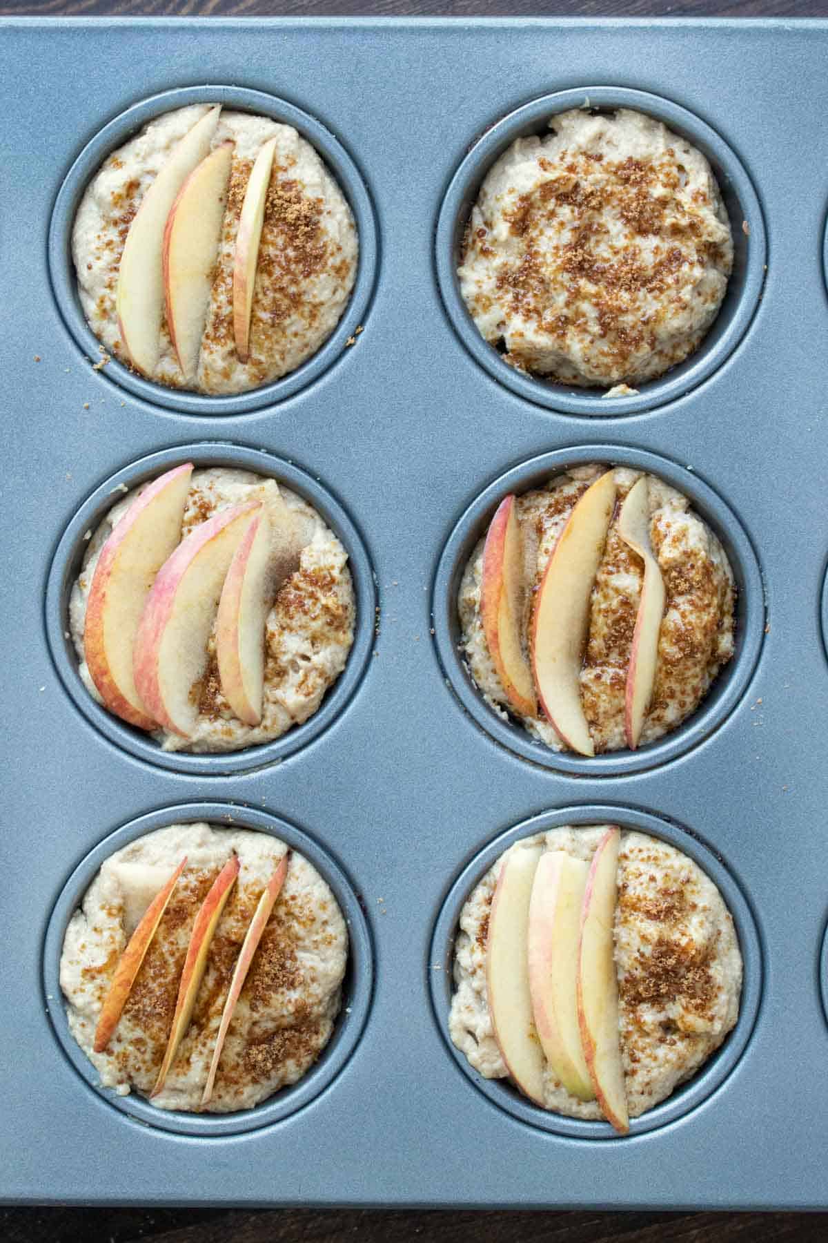 Muffin tin with batter and sliced apples on the top.