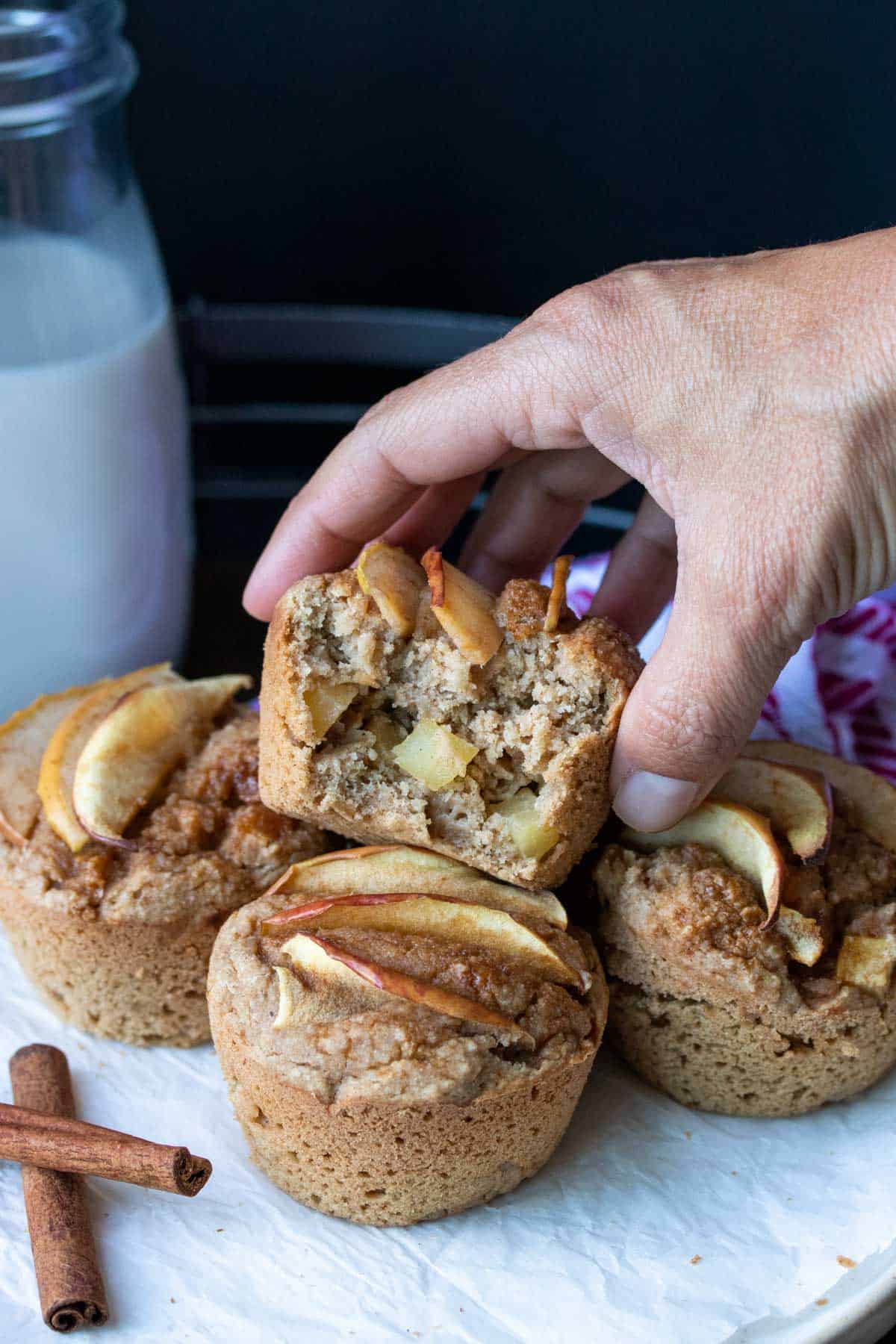 Hand grabbing a half eaten apple muffin from a pile.