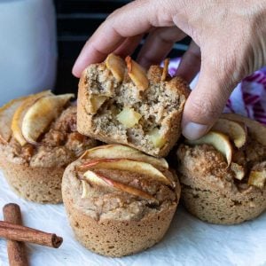 Half eaten apple muffin being grabbed of a pile of muffins.