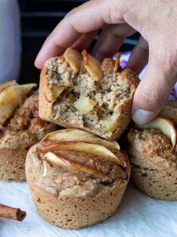 Half eaten apple muffin being grabbed of a pile of muffins.