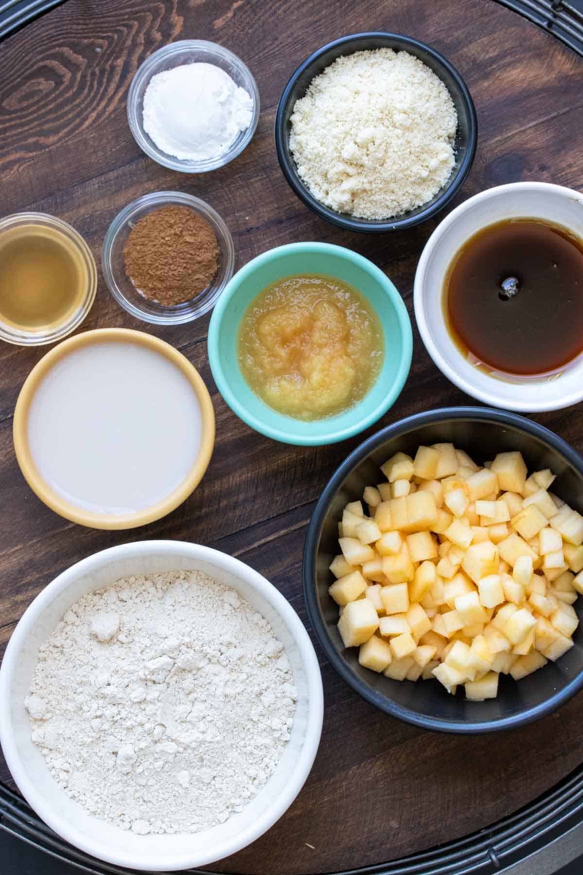 Different color and sized bowls with ingredients to make apple muffins in them.