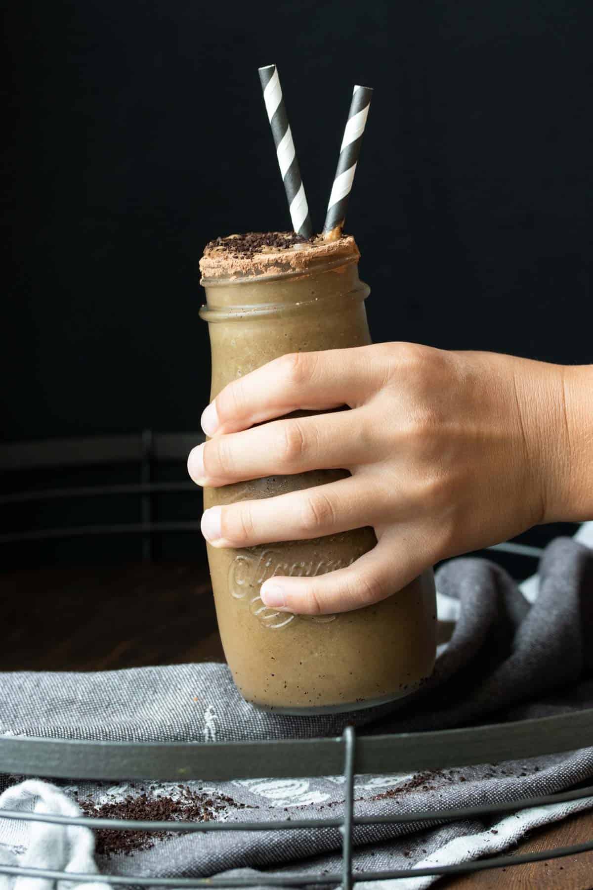 Hand grabbing a glass milk jar filled with a chocolate coffee smoothie.