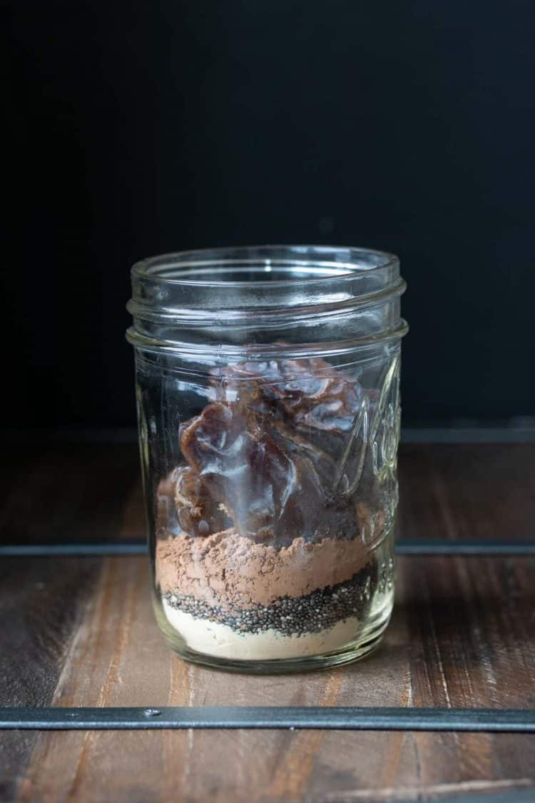 Glass jar filled with protein powder, espresso, cocoa and dates