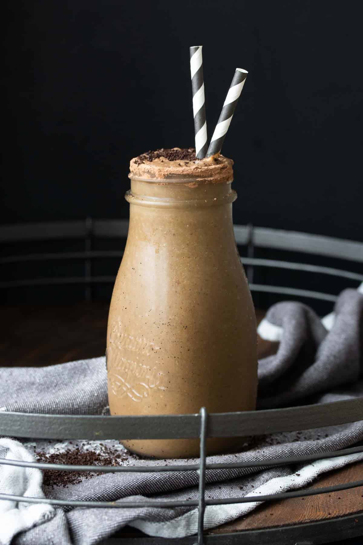 Chocolate coffee smoothie in a glass milk jar with two striped straws