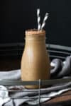 A coffee smoothie in a glass milk jar on a tray with two black and white straws in it.