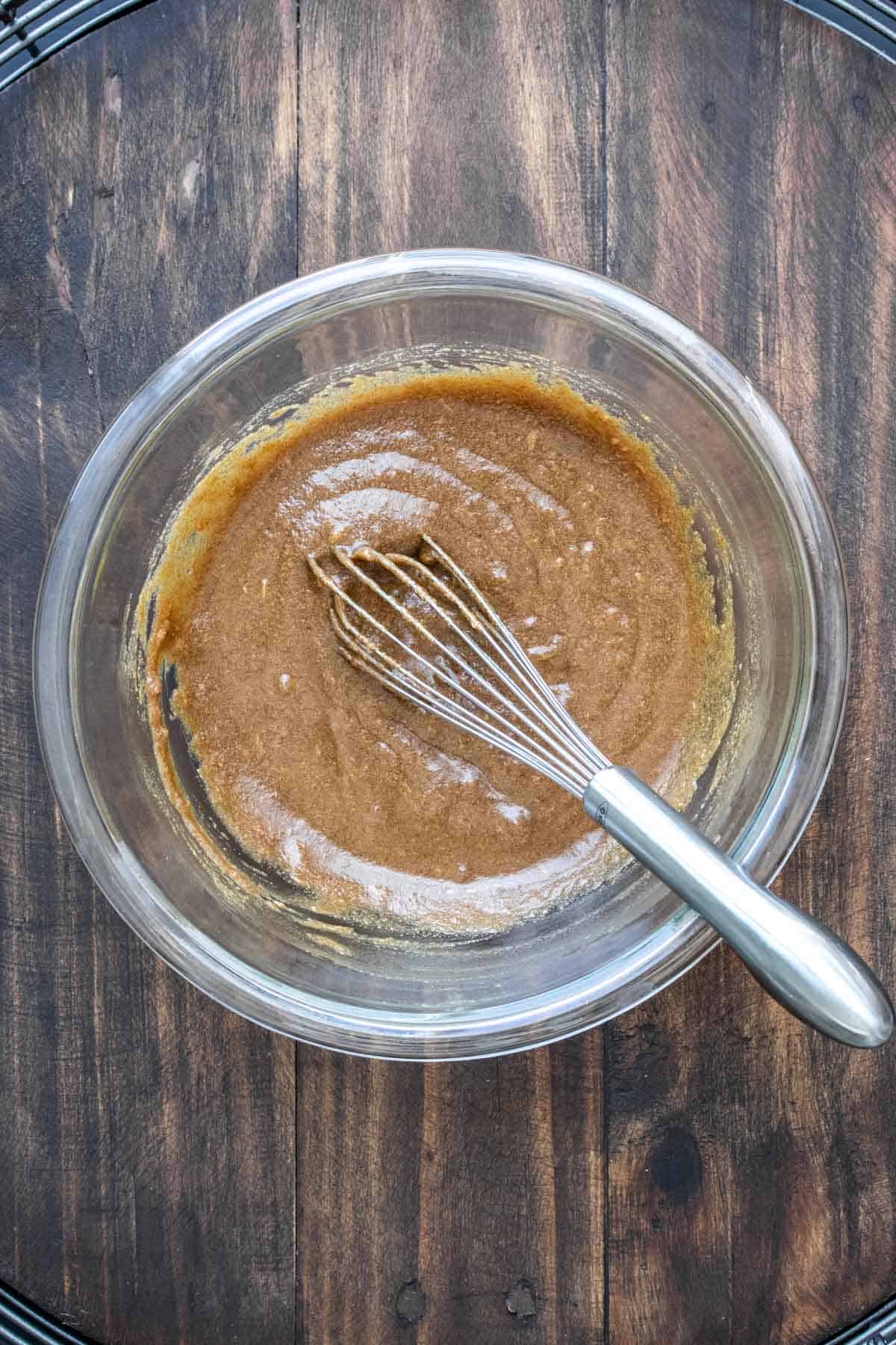 Whisk mixing a brown mixture in a glass bowl