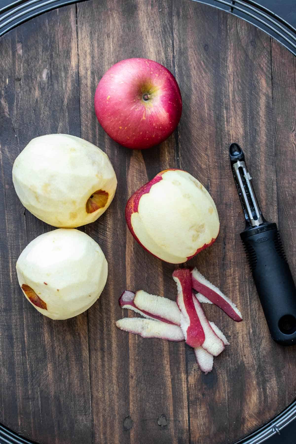 Four apples being peeled with a vegetable peeler