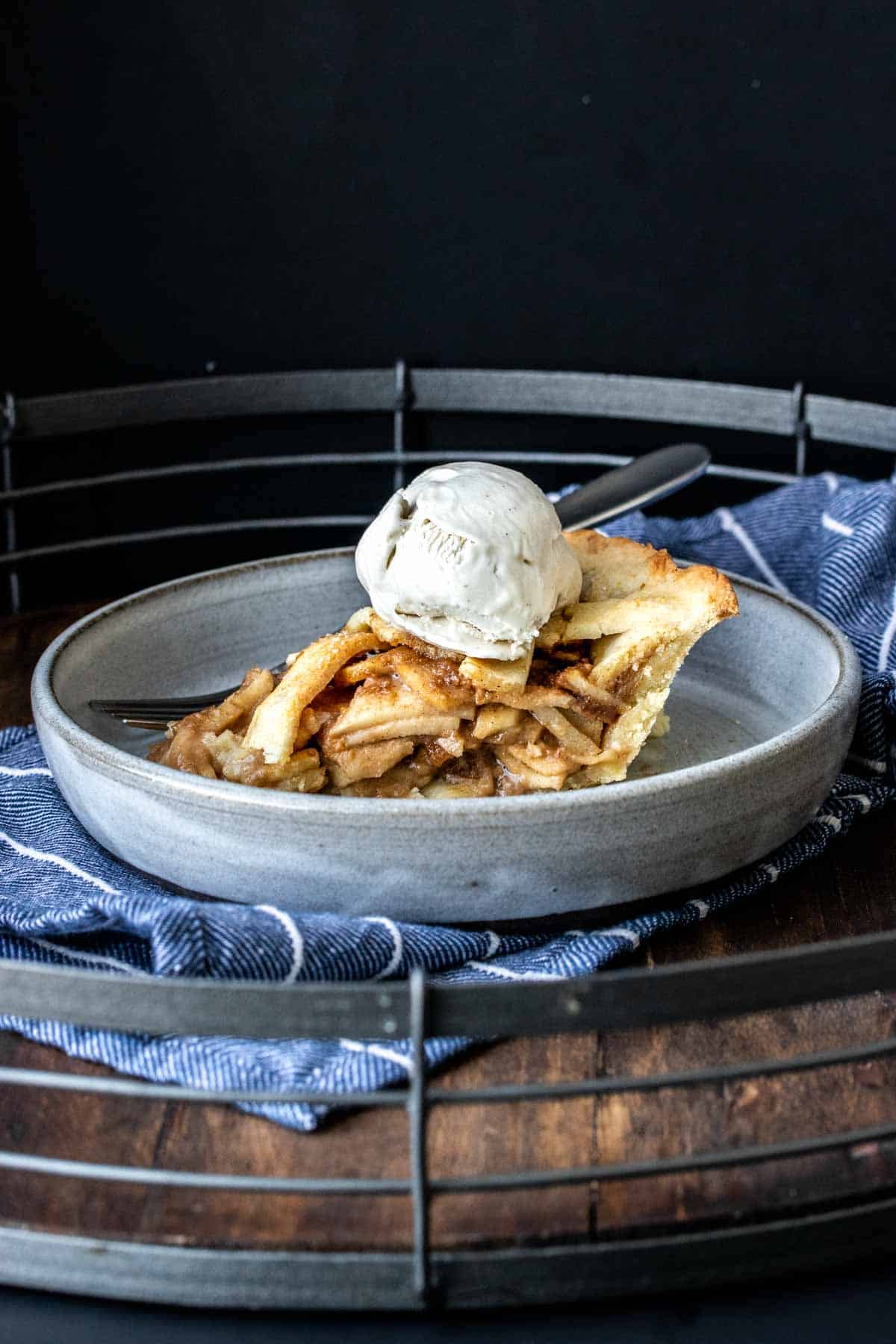 A piece of apple pie topped with ice cream on a grey plate.