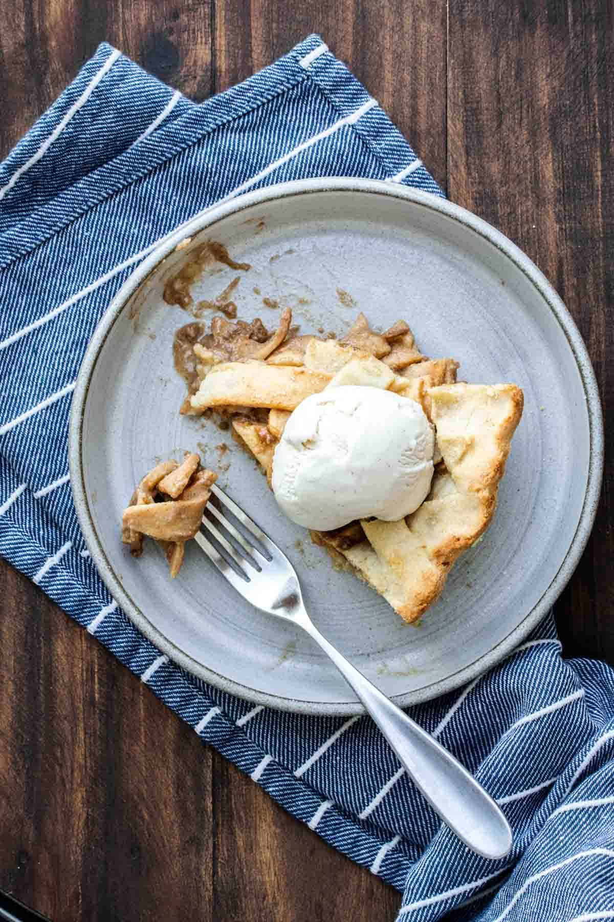 Top view of a fork eating a piece of apple pie topped with ice cream.