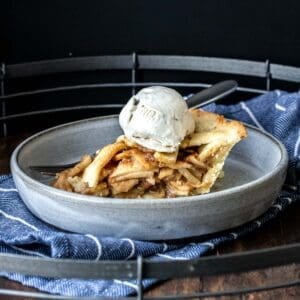 A side view of a piece of lattice covered apple pie with ice cream on top.