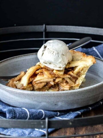 A side view of a piece of lattice covered apple pie with ice cream on top.