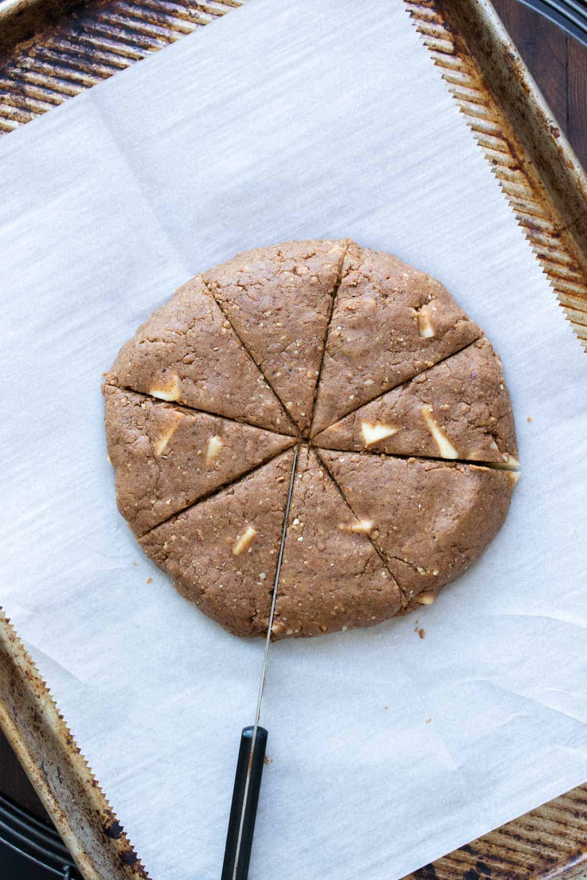 Knife cutting a circular shaped brown dough with apple pieces in it