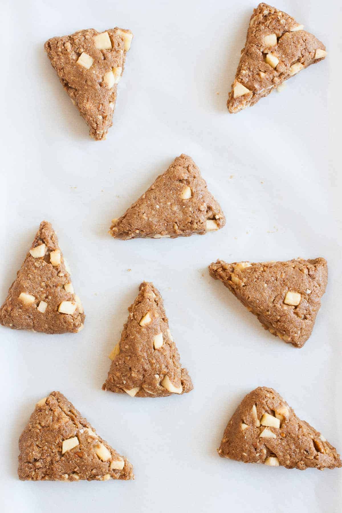 Eight raw apple scones on parchment paper ready to be baked