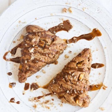 Two triangle shaped apple scones on a white plate with glaze drizzle