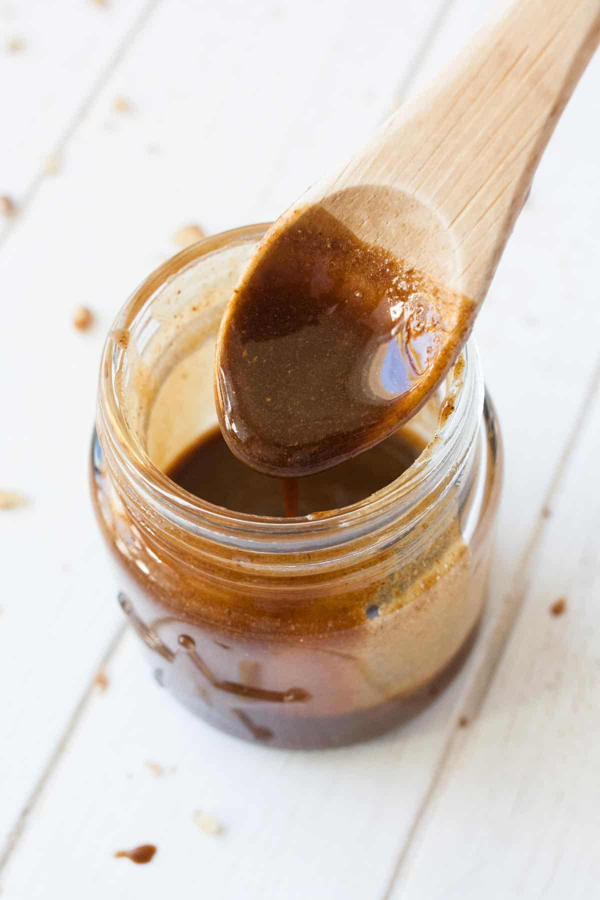Wooden spoon dipping into a glass jar of brown glaze