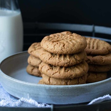 Grey plate with a pile of peanut butter cookies on it next to a glass of milk