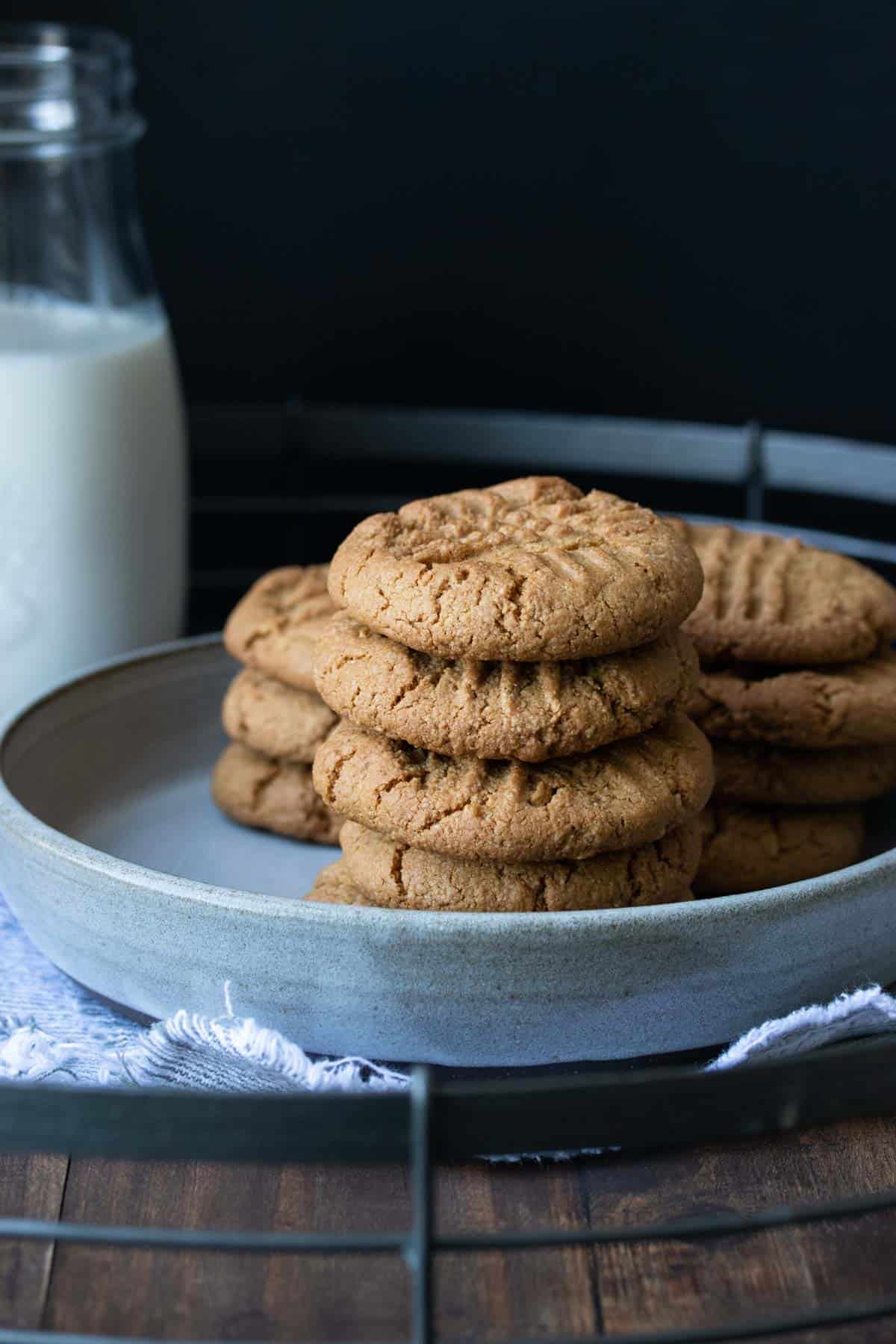 Grey plate with a pile of peanut butter cookies on it next to a glass of milk