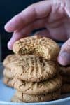 Hand holding a bitten peanut butter cookie over a pile of them