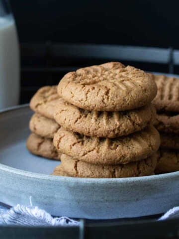Grey plate piled with stacks of peanut butter cookies next to a glass of milk