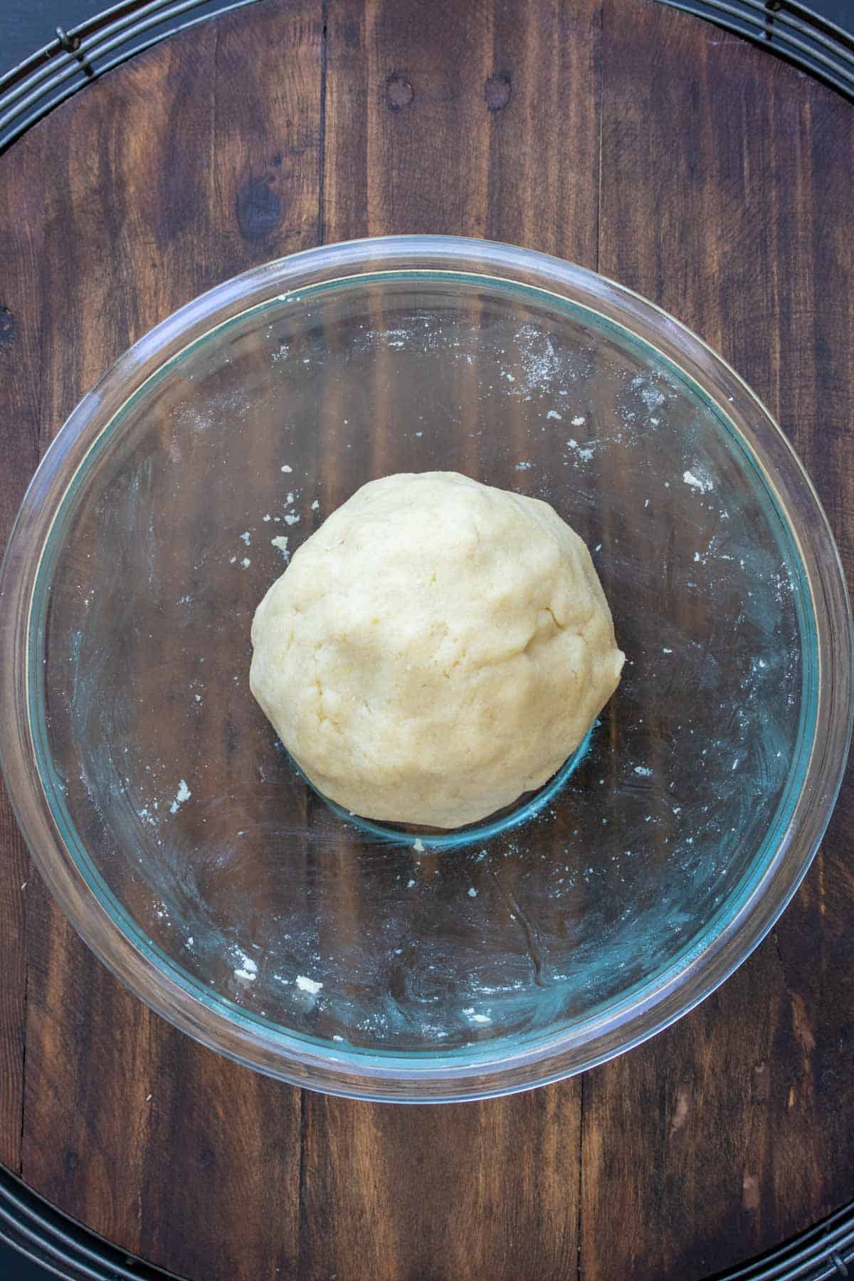 Pie dough ball in a glass bowl on a wooden table