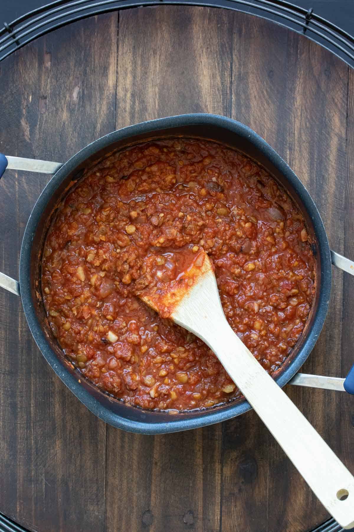 Wooden spoon mixing a bean based marinara in a pot