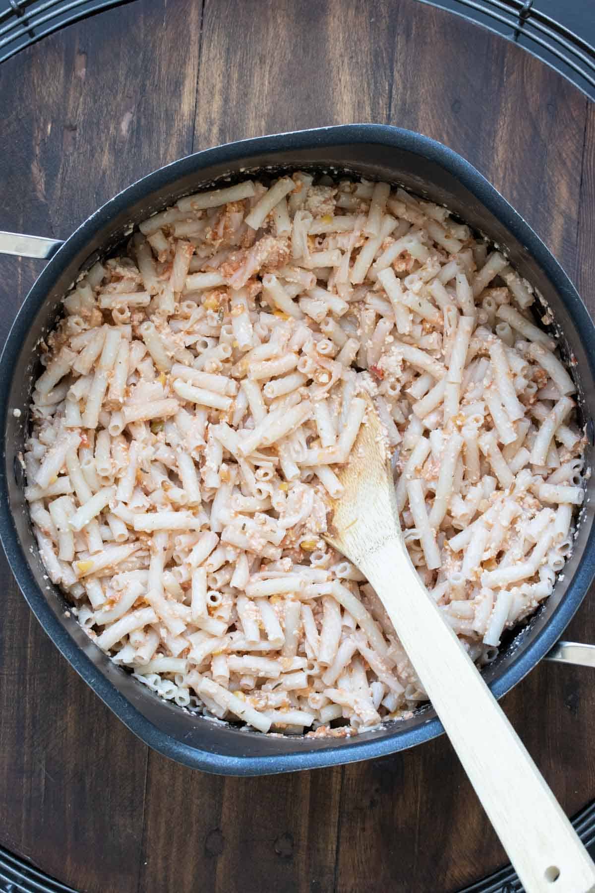 Pasta with a touch of sauce in a pot being mixed by a wooden spoon