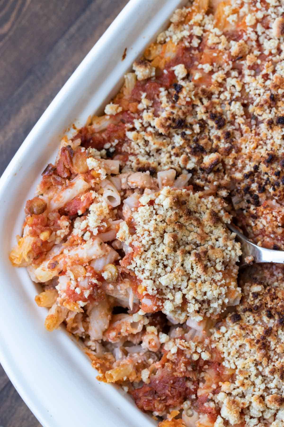 Spoon getting a scoop of baked pasta with sauce and parmesan from a baking dish