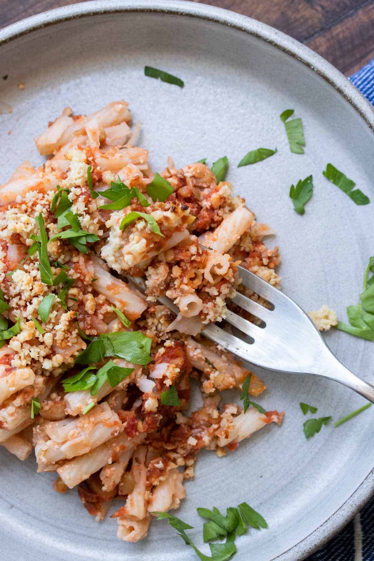 Fork taking a bite of baked pasta sprinkled with fresh parsley